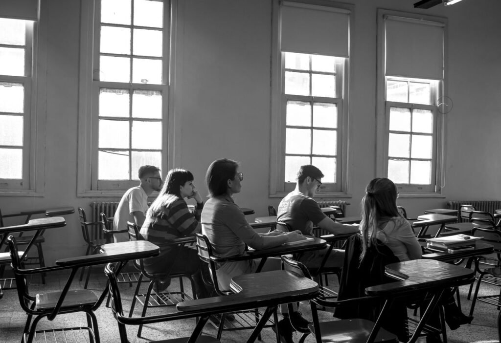 A group of students attentively listening in a classroom on a bright day.